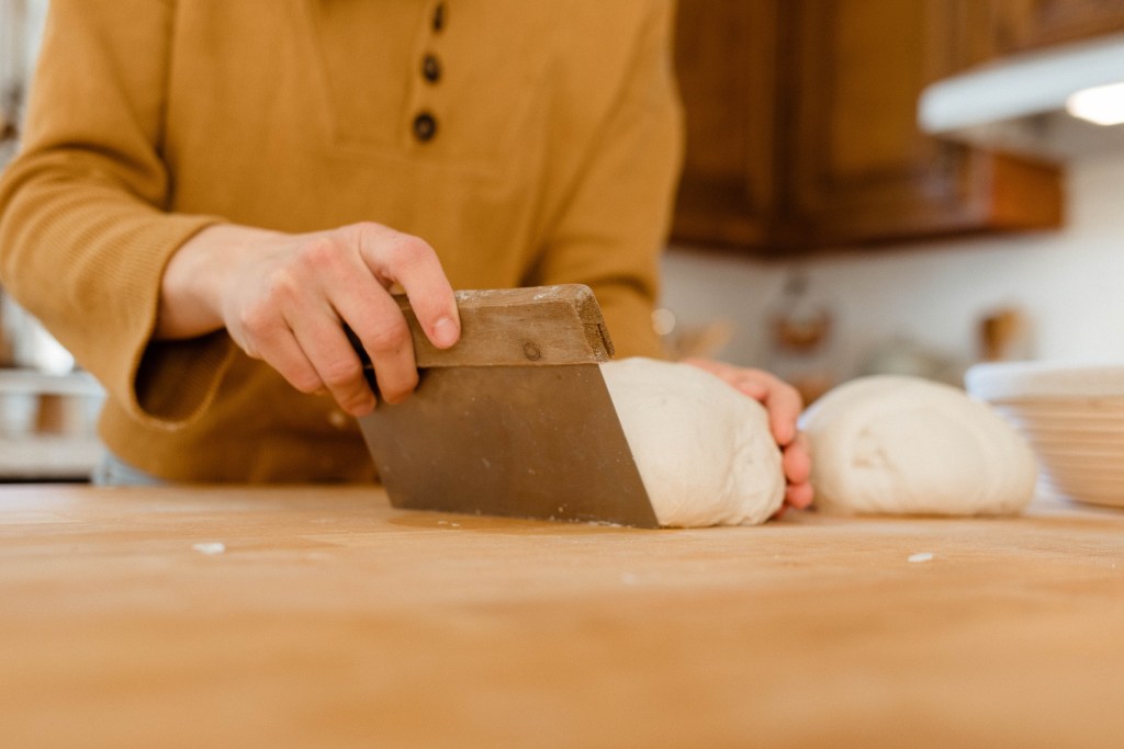 Girl using a bench scraper to scoop up her sourdough bread dough.